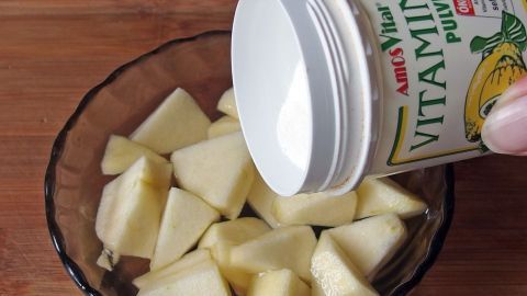 Gehackte Äpfel werden in eine Schüssel gegeben, während Vitamin C aus einem Behälter darüber gestreut wird, um Bräunung zu verhindern.