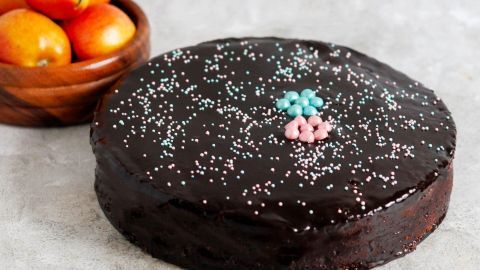 Eine Schoko-Apfel-Kuchen steht auf einer grauen Oberfläche, dekoriert mit bunten Streuseln und umgeben von frischen Äpfeln.
