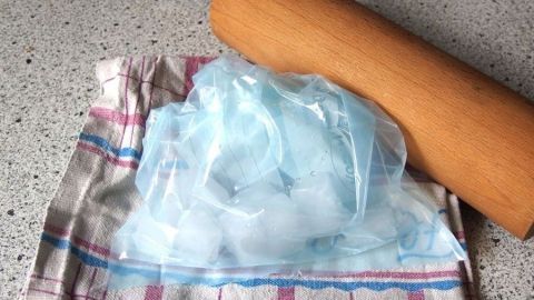 Eiswürfel liegen in einem Küchentuch, während ein Nudelholz zum Zerkleinern daneben bereitliegt.