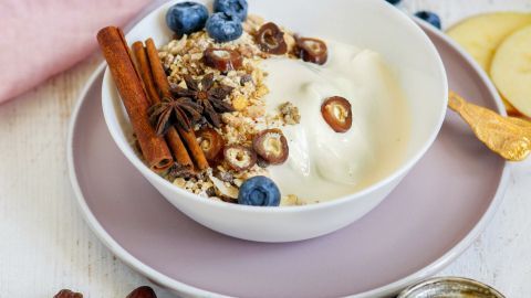 Ein Müsli-Kreis in einer Schüssel wird mit Joghurt, Zimt und frischen Heidelbeeren dekoriert und liegt auf einem gedeckten Tisch.