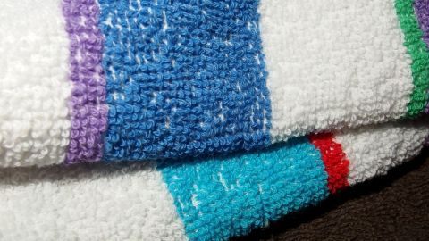 Halte deine Füße warm mit einem einfachen Tipp: Rubbel sie mit einem Frottiertuch. Die weiche Textur des bunten Handtuchs im Bild eignet sich perfekt, um die Durchblutung anzuregen und Kälte zu vertreiben. Ein Frottiertuch mit bunten Streifen liegt gefaltet auf einem Tisch, die Textur ist deutlich sichtbar.
