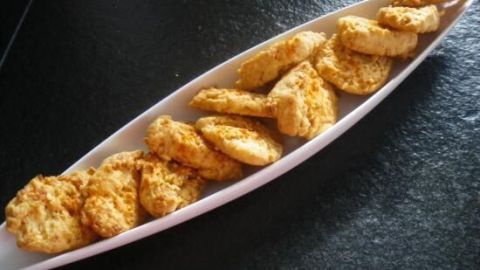 Käse-Cracker liegen auf einem langen, schmalen Teller und sind bereit zum Dippen in eine Sauce auf einem dunklen Tisch.