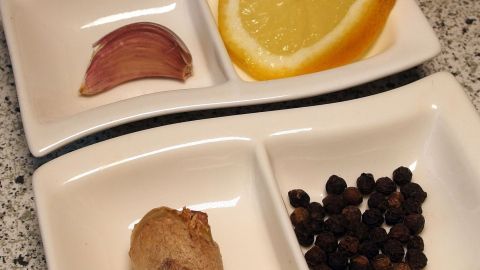 In zwei Schalen liegen frische Zutaten: eine Knoblauchzehe, Ingwerstück, schwarze Pfefferkörner und eine Orangenscheibe, die den Stoffwechsel anregen.