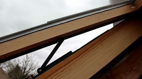 Holz-Dachfenster mit Flachpinsel streichen, für ein problemloses streichen auch an der Glasscheibe. Holzfenster wird mit einem Flachpinsel gestrichen, während graue Wolken im Hintergrund sichtbar sind.