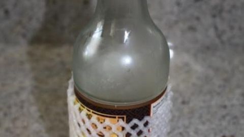 Eine Ölflasche, geschützt durch ein weißes Netz, steht auf einer Granit-Arbeitsplatte, möglicherweise um Klebrigkeit zu vermeiden.