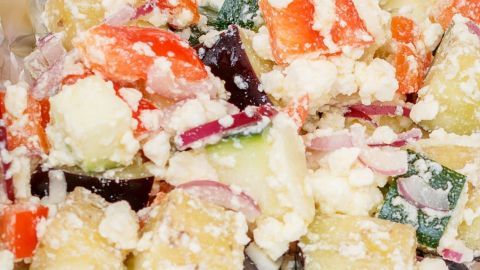 Ein bunter Gem&uuml;sesalat mit Feta und Zwiebeln, angerichtet in silberner Folie, bildet ein frisches, cremiges Ensemble.