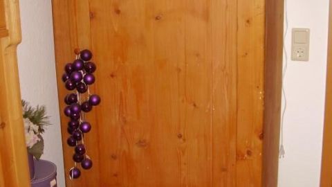 Ein Weichholzschrank steht still im Wohnzimmer, dekoriert mit lila Kugeln, umgeben von Holzboden und Wänden.