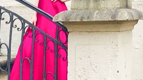 Ein elegantes Abendkleid wird von einer Frau auf einer Treppe präsentiert, umgeben von einer hellen, neutralen Mauer.