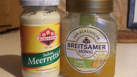Ein Glas Meerrettich steht neben einem Honigglas auf einer Küchenoberfläche, umgeben von einer warmen, hölzernen Umgebung.
