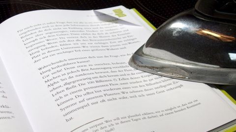 Ein offenes Buch liegt auf einem Tisch, während ein Dampfbügeleisen über die Seiten gleitet, um Knicke zu entfernen.