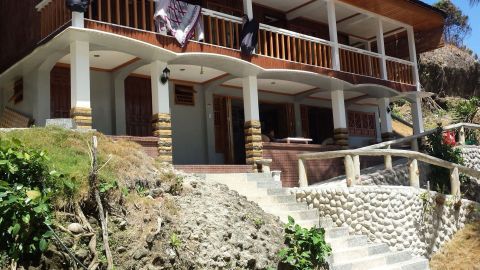 Ein einladendes Unterkunftsgebäude steht in der Sonne, umgeben von grüner Vegetation, ideal für Couchsurfing während des Urlaubs.