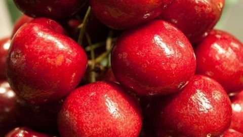 Leuchtend rote Kirschen stapeln sich pyramidenartig in Nahaufnahme auf einem Marktstand, glänzend in warmem Licht.