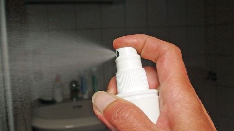 Eine Hand hält eine Sprühflasche, die feinen Duft ausstößt, um einen frischen Raum in einem Badezimmer zu schaffen.