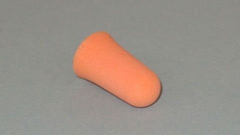 Ein orangefarbener Ohrenstöpsel liegt auf einem grauen Hintergrund, bereit zur richtigen Platzierung im Ohr für Ruhe.