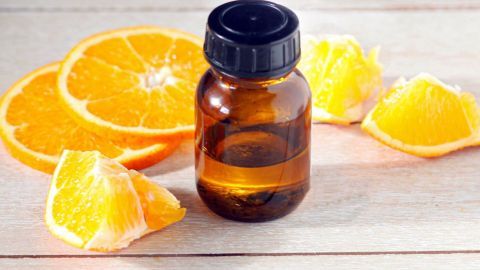 Ein Glasfläschchen mit Orangenöl steht auf einer Holzoberfläche, umgeben von frischen Orangenscheiben und -stücken.