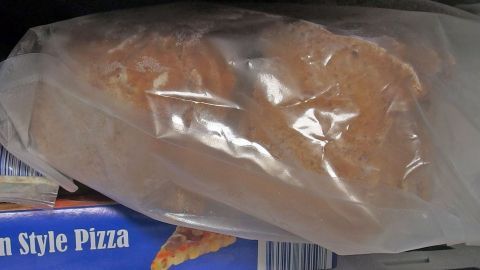 Eine Tüte mit gefrorenem Brot liegt im Gefrierfach, um frische Auswahl zu bieten, während Tiefkühlpizza daneben liegt.
