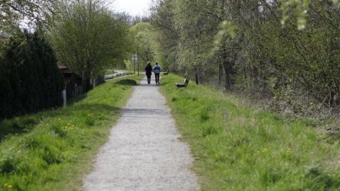Eine gravel path erstreckt sich durch eine grüne Landschaft, während zwei joggende Personen in der Ferne unterwegs sind.