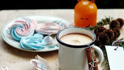 Ein Keramikbecher mit Kinderpunsch steht auf einem Tisch, umgeben von bunten Süßigkeiten und festlicher Dekoration.