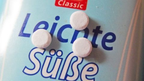 Weiße Süßstofftabletten liegen auf einer blauen Verpackung mit dem Text "Leichte Süße" im Fokus.