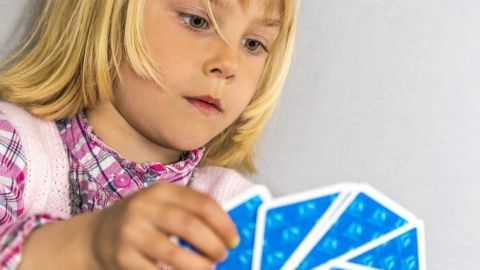 Kind hält blaue Spielkarten in der Hand, konzentriert in neutralem Hintergrund.