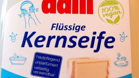 Flüssige Kernseife aus Dalli steht im Vordergrund, um Flecken zu entfernen, umgeben von Wasser-Illustrationen.