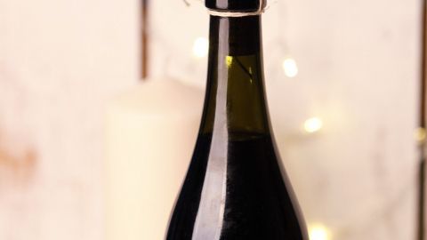 Eine schwarze Weinflasche mit einem feststeckenden Korken steht vor einem Kerzenlicht, bereit geöffnet zu werden.