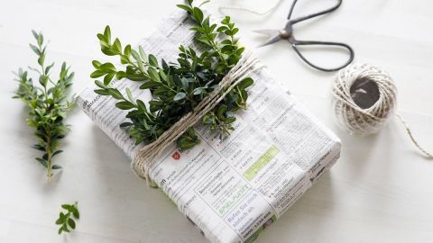 Ein schön verpacktes Geschenk in Zeitungspapier liegt auf einem Tisch, dekoriert mit frischen Zweigen und Schnur.