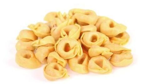 Tortellini liegen gestapelt auf einer weißen Oberfläche und zeigen ihre goldene Farbe im einfachen Studiolicht.
