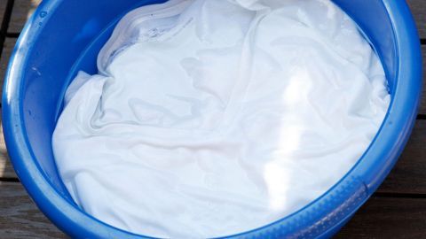 Ein blauer Eimer enthält ein gewaschenes, weißen T-Shirt, das darauf hinweist, wie eingelaufene T-Shirts verhindert werden können.