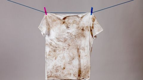 Ein verschmutztes, altes T-Shirt hängt an einer Wäscheleine, während es gewaschen wird, um die Flecken zu entfernen.