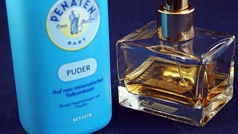 Mein Tipp: Man nehme Babypuder, tue davon ca. 1 Teelöffel in ein Gefäß, darauf 7 Tropfen von deinem Lieblingsparfüm, verrühren. Wenn das trocken ist, mit einem Holzstiel wieder pudrig stoßen, zurück zum Babypuder, gut schütteln, fertig. Ein blauer Körperpuder und eine elegante Parfumflasche stehen nebeneinander auf einem dunklen Untergrund.