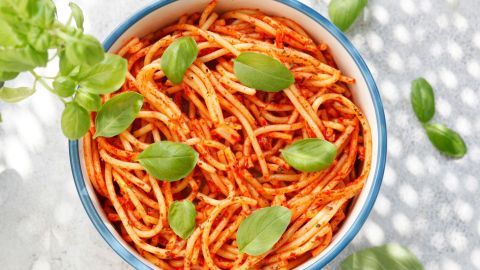 Spaghetti in einer Schüssel werden mit frischen Basilikumblättern garniert und sind unter einem hellen Licht platziert.