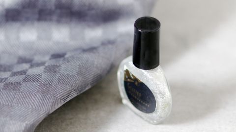 Ein Glitzernagellack steht auf einem hellen Tisch neben einem grauen, gemusterten Stoff, bereit zum Entfernen.