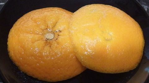 Zwei orangefarbene Zitrusschalen liegen übereinander auf einem schwarzen Teller, bereit zur Dekoration und kreativen Verwendung.