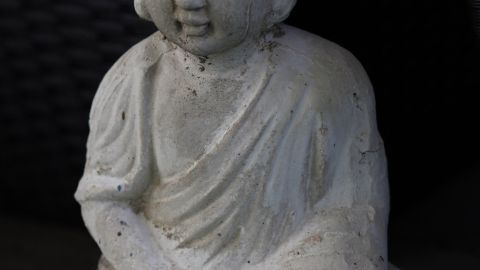 Eine Buddha-Statue sitzt ruhig im Schneidersitz auf grünem Untergrund und strahlt Entspannung und Gelassenheit aus.