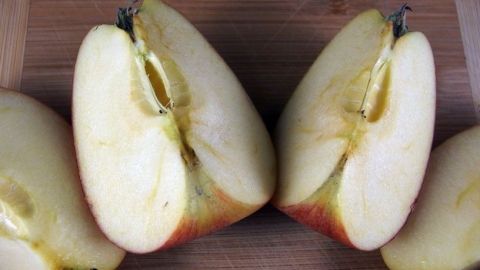 Zwei halbierte Äpfel liegen auf einem Holzbrett, die Schnittflächen zeigen nach oben, bereit, für Gesichtspflege verwendet zu werden.