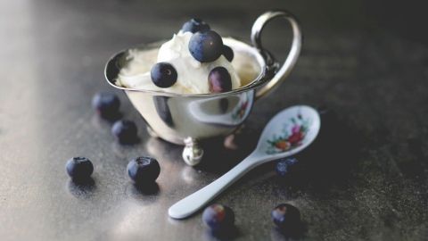 Ein silbernes Schälchen mit Eis und Blaubeeren wird auf einer dunklen Oberfläche präsentiert, umgeben von frischen Blaubeeren.