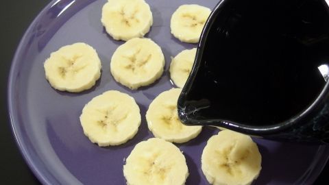Gesunde Schleckerei - Bananenscheiben mit O-saft beträufeln und auf einem Teller gefrieren lassen. Gefrorene Bananenscheiben liegen auf einem lila Teller, während eine schwarze Kanne Likör darüber gegossen wird.