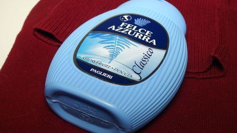 Zum Waschen von Wolle kann man anstatt Wollwaschmittel Duschgel verwenden. Ein Flasche Wollwaschmittel liegt auf einem roten Pullover, bereit zum Waschen, um die Kleidung zu schonen.