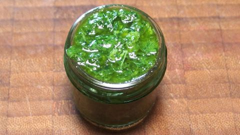 Ein Glas mit grünem Pesto steht auf einem Holzbrett. Es wirkt frisch und selbst gemacht, bereit zum Servieren.