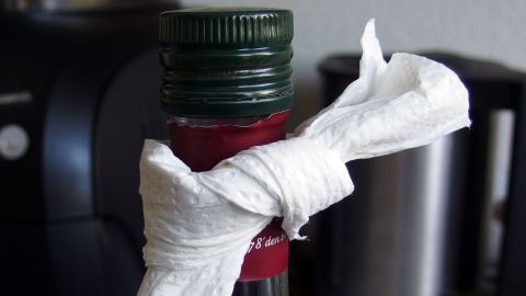 Knote ein Stück Küchenpapier unter den Flaschenhals, um eine klebrige Ölflasche zu vermeiden. Eine Ölflasche mit einem grünen Deckel hat ein Papiertaschentuch um den Flaschenhals gewickelt, um Klebrigkeit zu vermeiden.