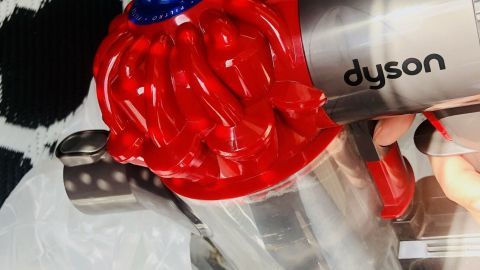 Beutellosen Staubsauger relativ sauber und staubfrei entleeren mithilfe einer alten Tüte. Ein beutelloser Staubsauger wird in die Tüte geleert, um den Schmutz zu entsorgen, auf einem gemusterten Teppich.