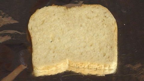Ein Stück Toastbrot liegt flach auf einem dunklen Tisch, bereit, ohne Toaster zubereitet zu werden.