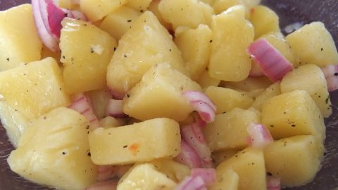 Ein bunter Kartoffelsalat mit gewürfelten Kartoffeln und roten Zwiebeln in einer Schüssel, frisch zubereitet.