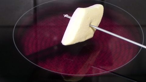 Ein Marshmallow wird auf einem Spieß über einer heißen Oberfläche geröstet, ideal für gegrillte Marshmallows ohne Lagerfeuer.