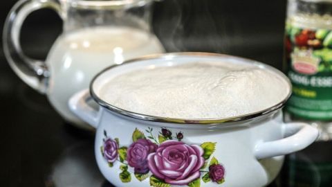Ein Topf mit übergekochter Milch dampft und hat einen kleinen Rand aus verschütteter Flüssigkeit auf der Kochplatte.