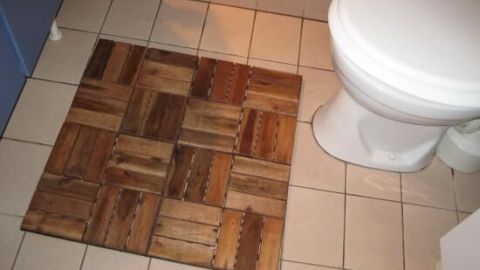 Holzfliesen liegen vor einer Toilette auf beigen Fliesen, schaffen eine warme, natürliche Atmosphäre im Badezimmer.