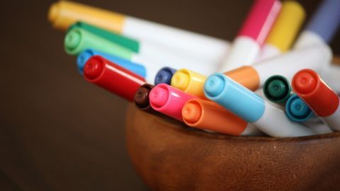 Filzstifte ragen in verschiedenen Farben aus einer hölzernen Schale auf einem dunklen Tisch heraus.