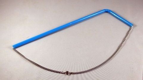 Ein blauer Schmuckhalter liegt auf einem Tisch und hält eine Schmuckkette offen, um Verwicklungen zu vermeiden.