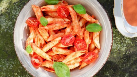 Ein Gericht mit Penne, überzogen mit einer Tomaten-Sahne-Sauce, garniert mit Kirschtomaten und frischem Basilikum.